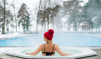 Young blonde woman in red hut in bathtub jacuzzi outdoors at winter day
